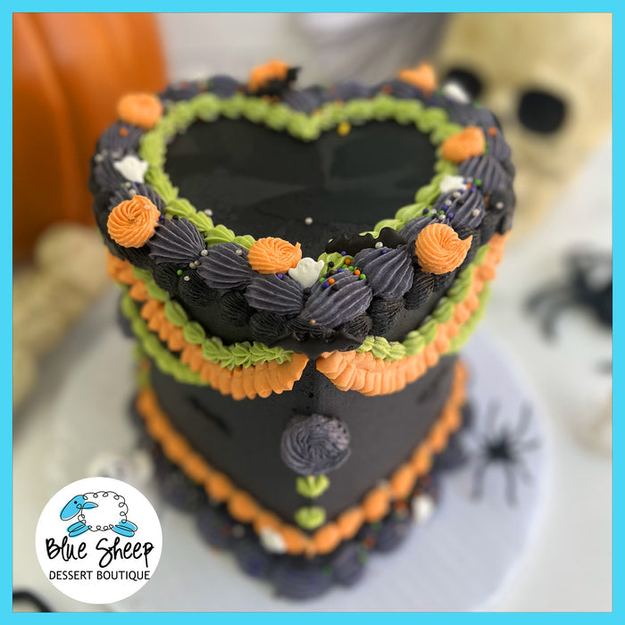 Lambeth style Halloween cake, heart-shaped bakery cake with black buttercream, and piping in green, orange, and grey tones. Decorated with Halloween themed sprinkles and little sugar ghosts.