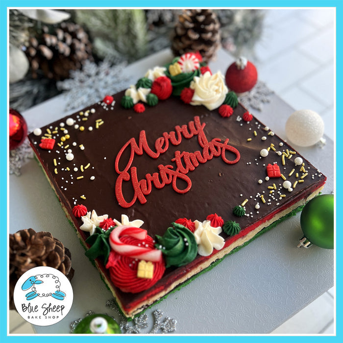 Italian Rainbow Cookie Cake with chocolate ganache and holiday decorations, featuring "Merry Christmas" lettering, from Blue Sheep Bake Shop.
