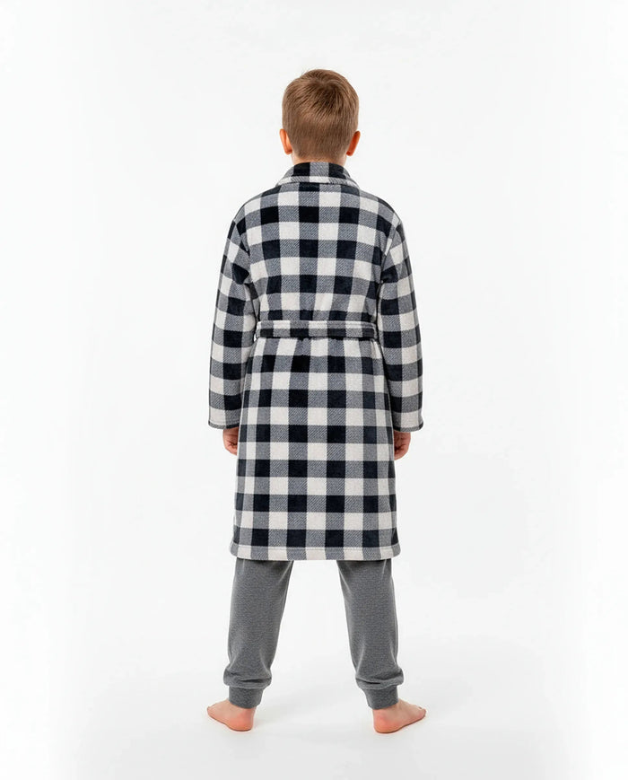 Niño de espaldas con cómoda bata a cuadros blanco y negro sobre pijama gris de terciopelo para invierno