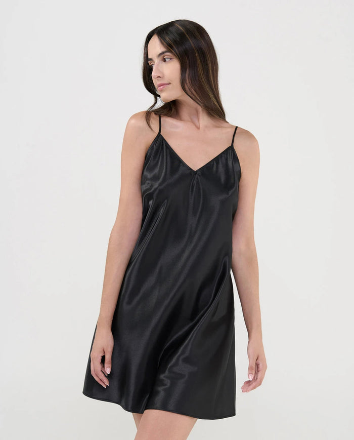 Mujer luce delicado camisón corto de raso negro, escote en pico y tirante fino