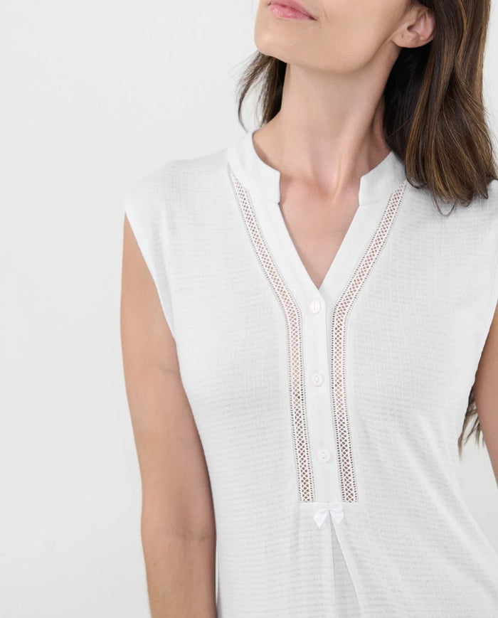 Detalle del cuello pata abotonado marfil con entredós y lazo decorativo.