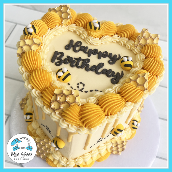 Bee-themed heart-shaped birthday cake with yellow buttercream swirls, honeycomb details, and fondant bees – Blue Sheep Bake Shop Somerville NJ