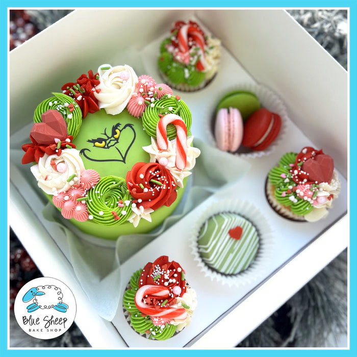 Grinch Christmas Gift Box featuring a Grinch-themed mini cake, 3 colorful French macarons, and a chocolate-covered macaron surrounded by holiday decorations