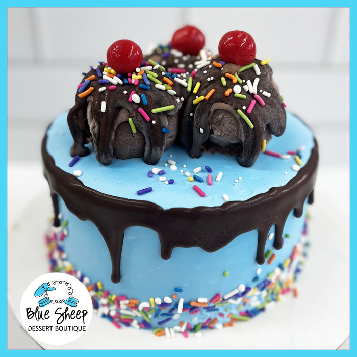 A vibrant blue ice cream birthday cake with sprinkles and a chocolate drizzle, topped with scoops of ice cream and a cherry.