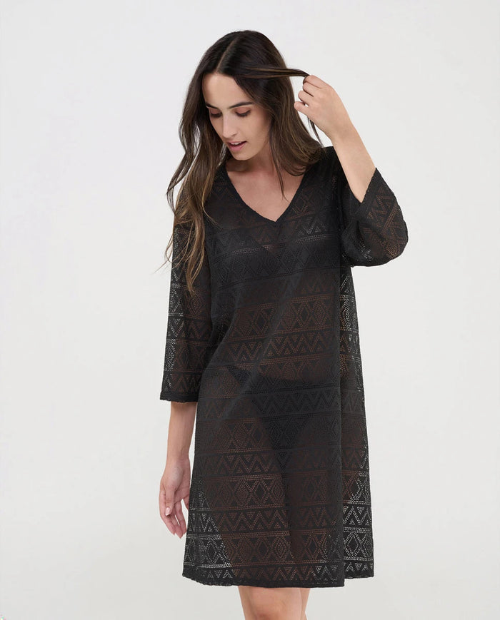 Mujer luce vestido negro corto de baño con manga en punto desagujado motivos geométricos con cuello pico.
